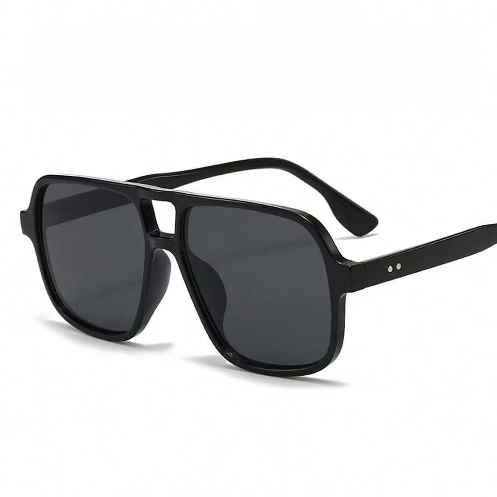 Black oversized aviator sunglasses with smoky gray lenses, a cutout bridge, and two small silver-tone dots on the temple against a white background