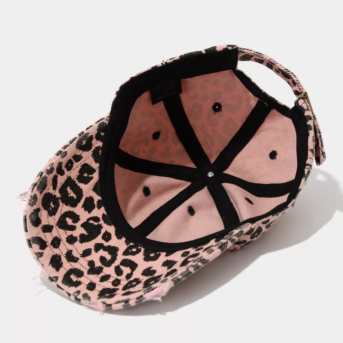 Interior view of a pink leopard print baseball cap showing black seam binding, inner band, eyelets, and adjustable back strap
