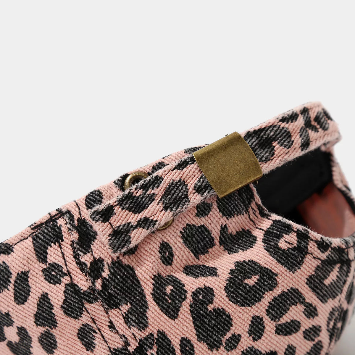 Close-up of the adjustable back strap on a pink cotton leopard print baseball cap, showing black spots and an antique brass-tone metal buckle