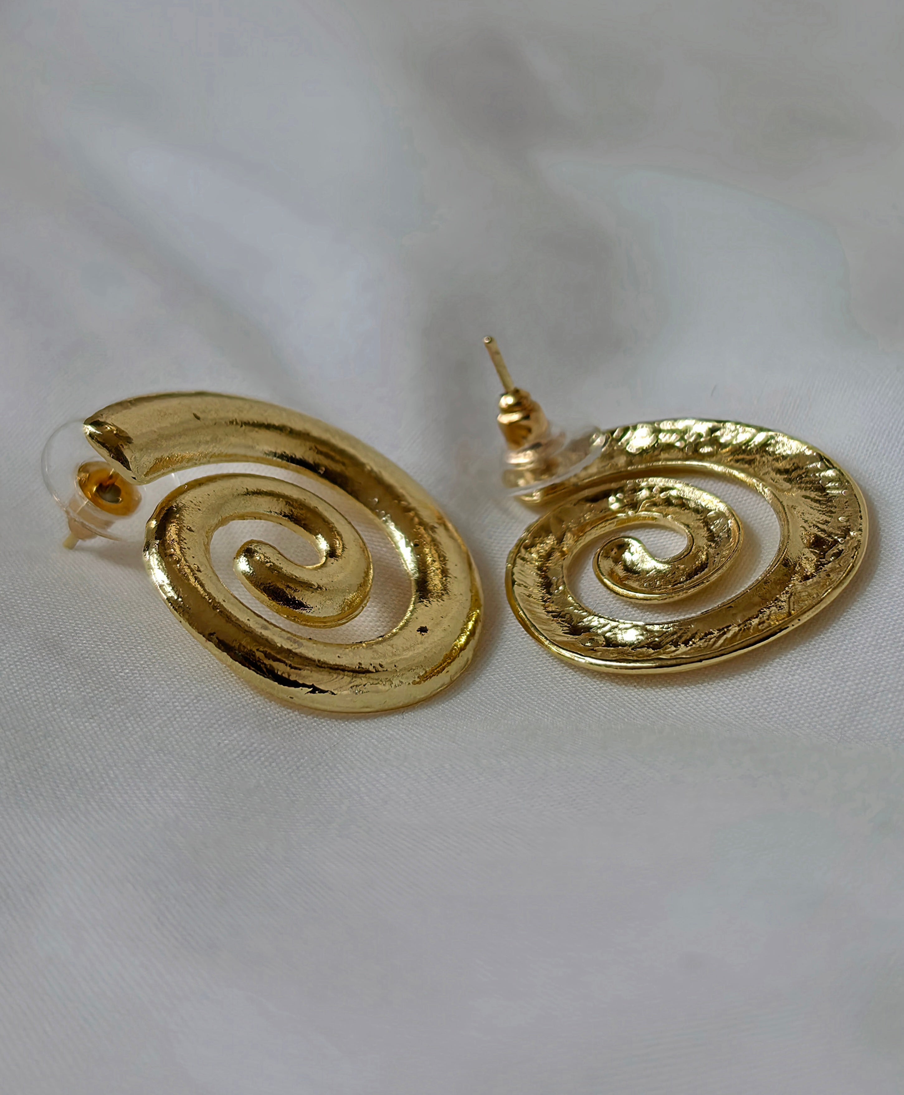 A pair of gold spiral drop earrings with a textured finish, displayed on a soft white fabric background.