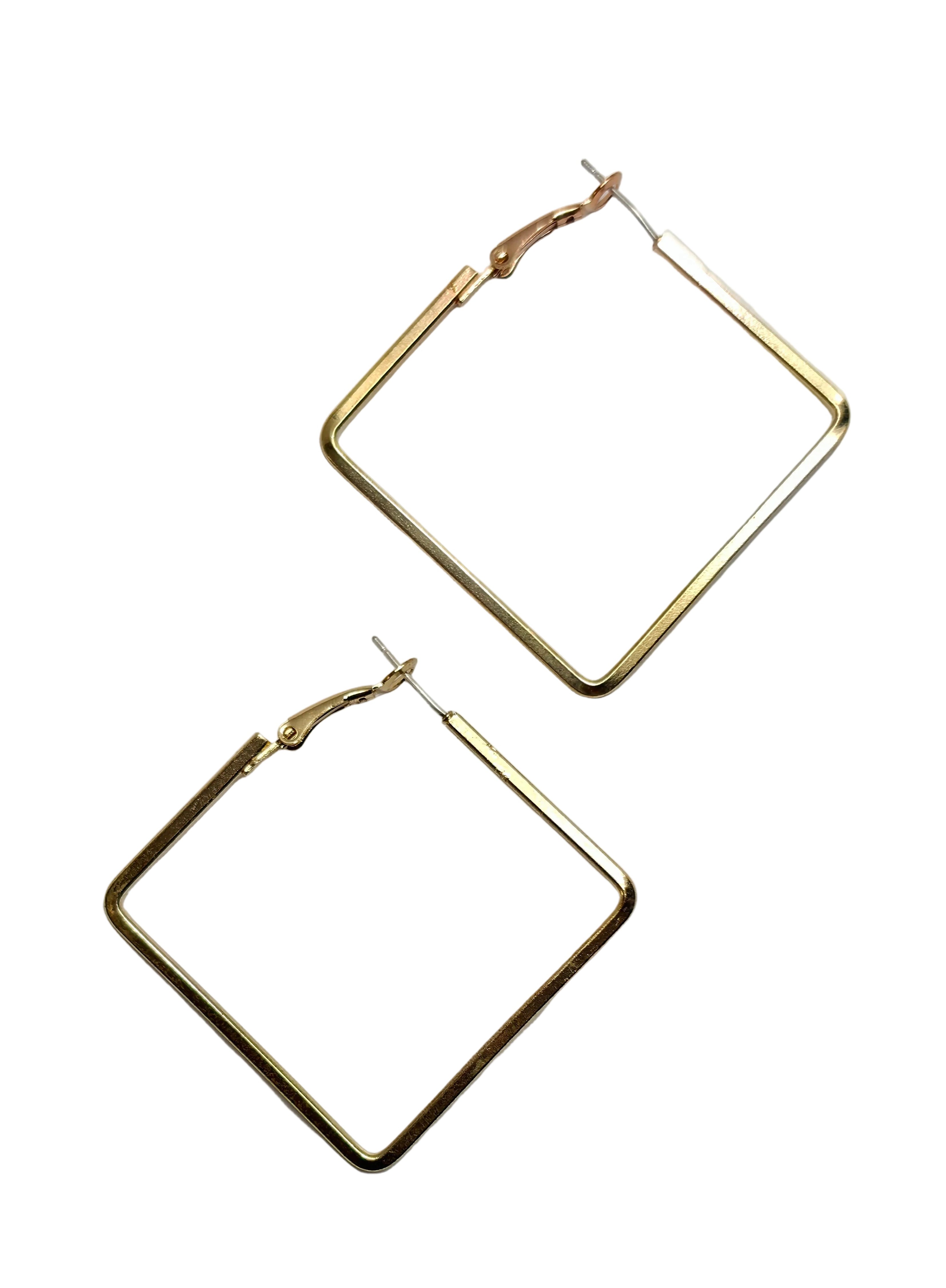 A pair of large, open-frame geometric hoop earrings in a polished gold-tone finish, displayed on a clean, light gray surface.