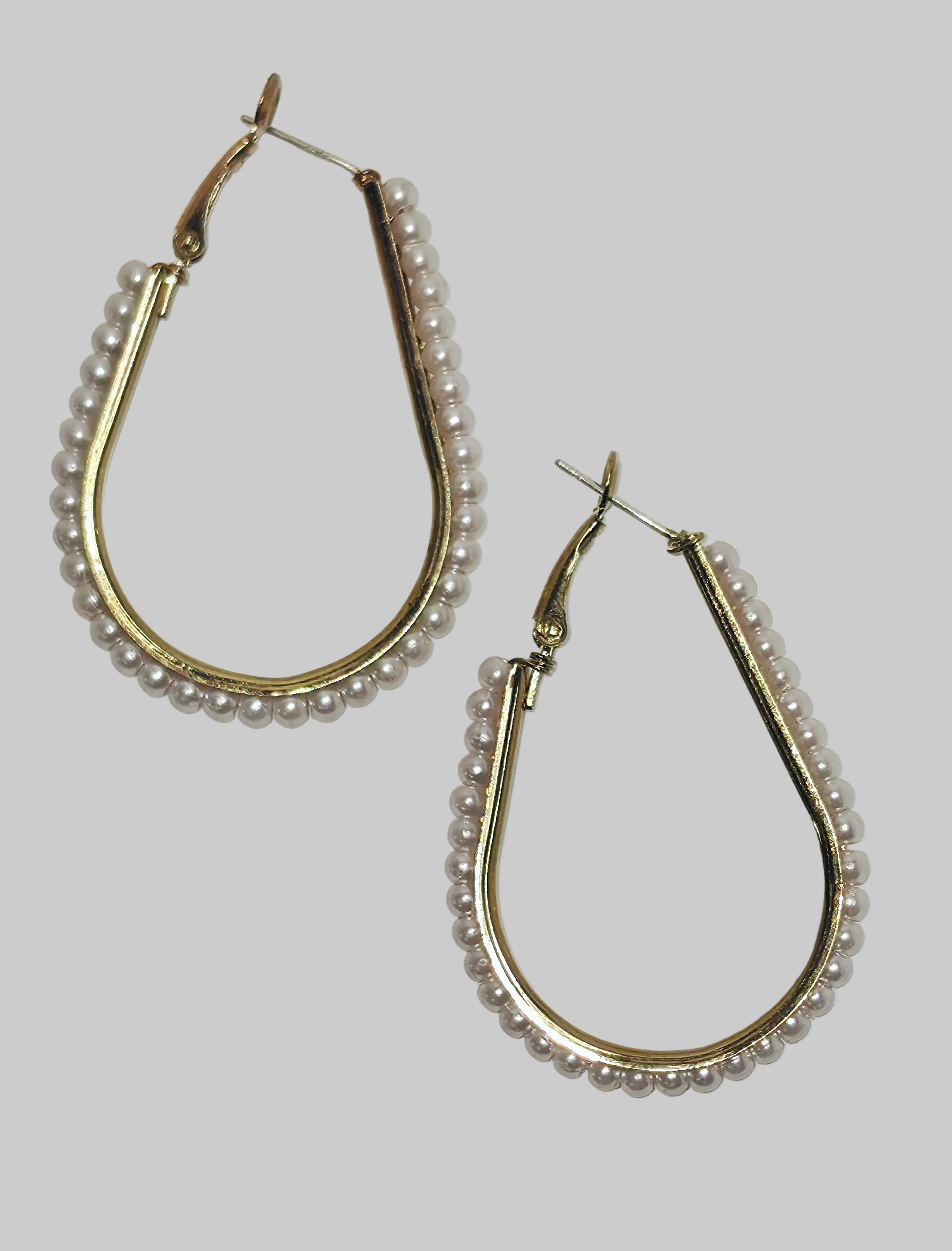 A pair of gold-tone teardrop hoop earrings decorated with small white pearls along the curved edges, displayed on a light gray background.