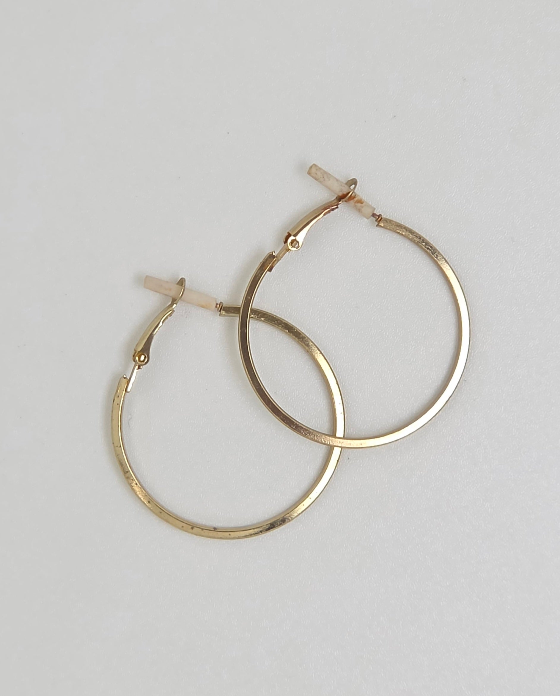 A pair of gold hoop earrings with a textured finish and leverback closures, displayed on a light gray background.