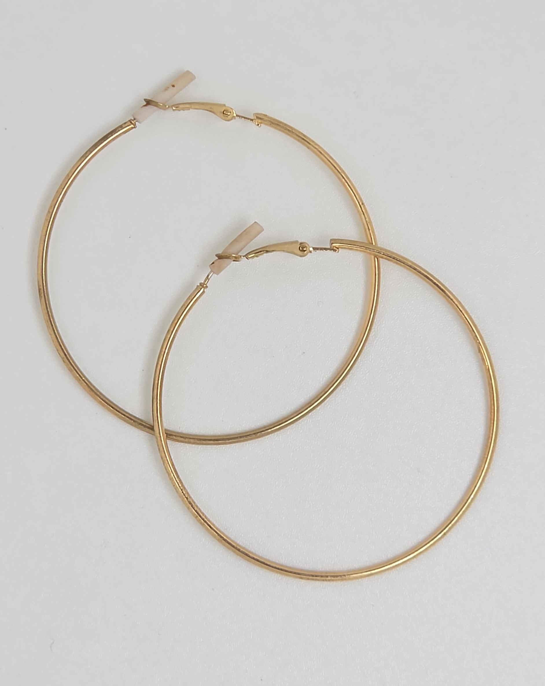 A pair of gold hoop earrings with a flat, textured finish and small rectangular huggie backings, displayed on a clean white background.
