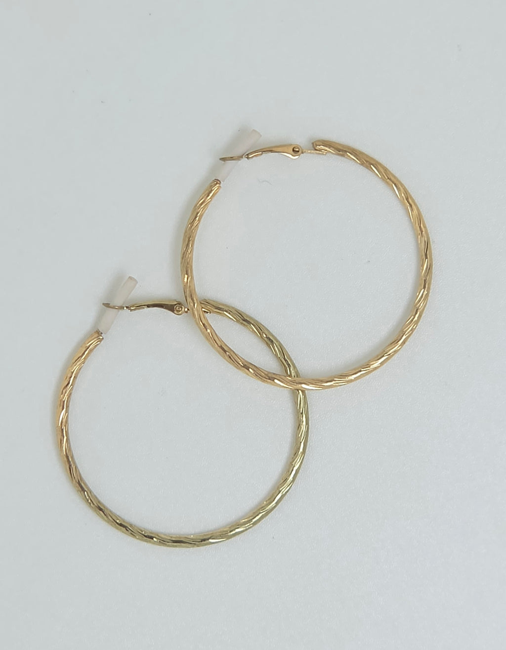 A pair of gold hoop earrings with a textured, twisted finish, displayed on a plain light gray background.