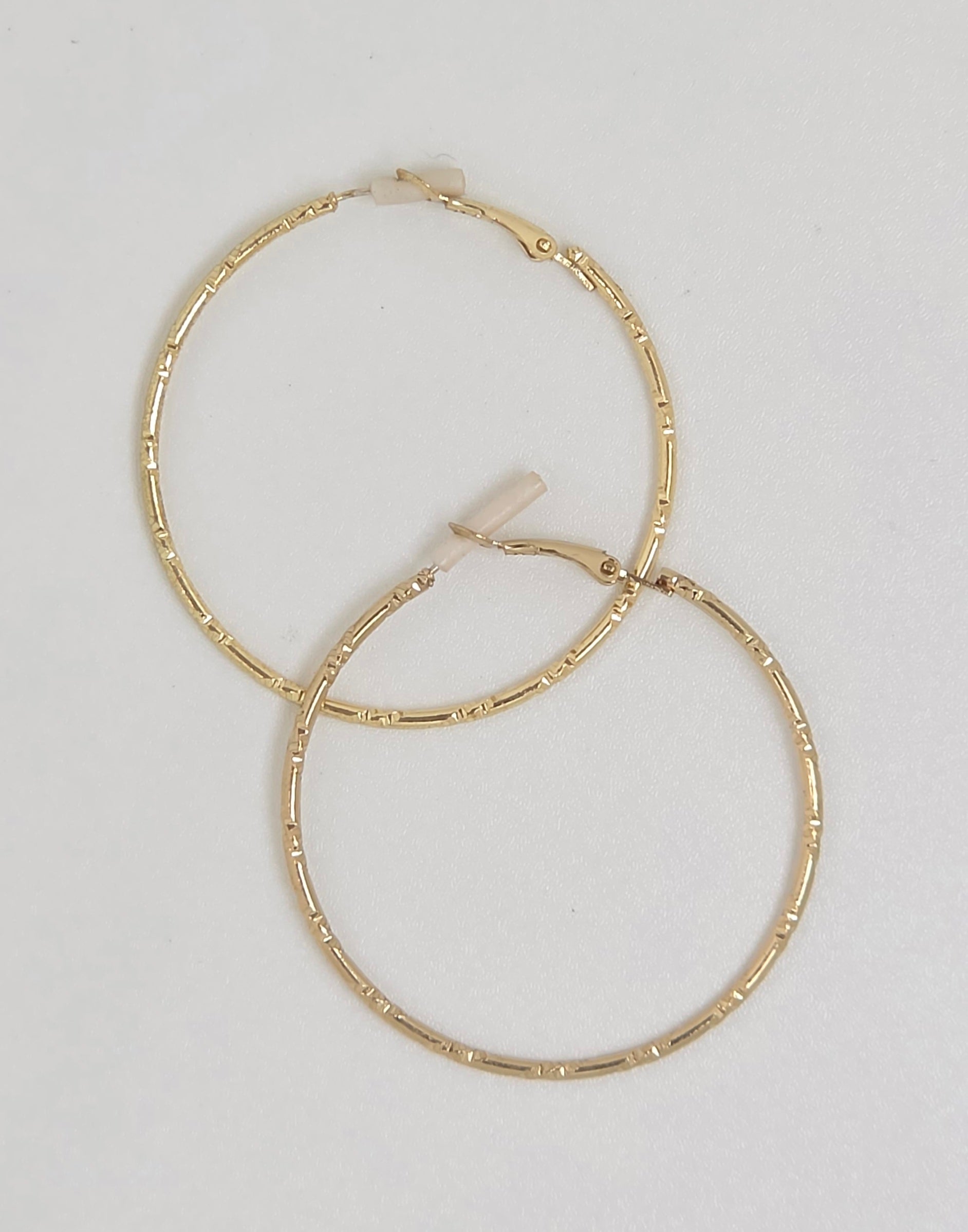 A pair of gold hoop earrings with a textured, segmented design, displayed on a plain off-white background.