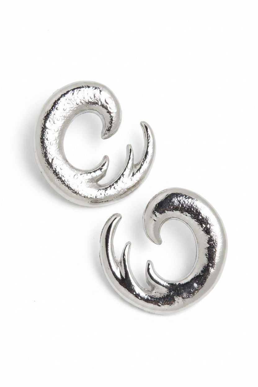 Pair of silver spiral swirl stud earrings displayed on pink diamond suede jewelry stand, close-up showing chunky sculptural open spiral design and high-polish silver-tone finish