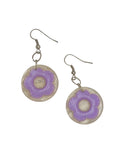 A pair of dangle earrings with circular clear resin pendants featuring a raised lavender purple flower in the center, suspended from silver fishhook wires on a white background.