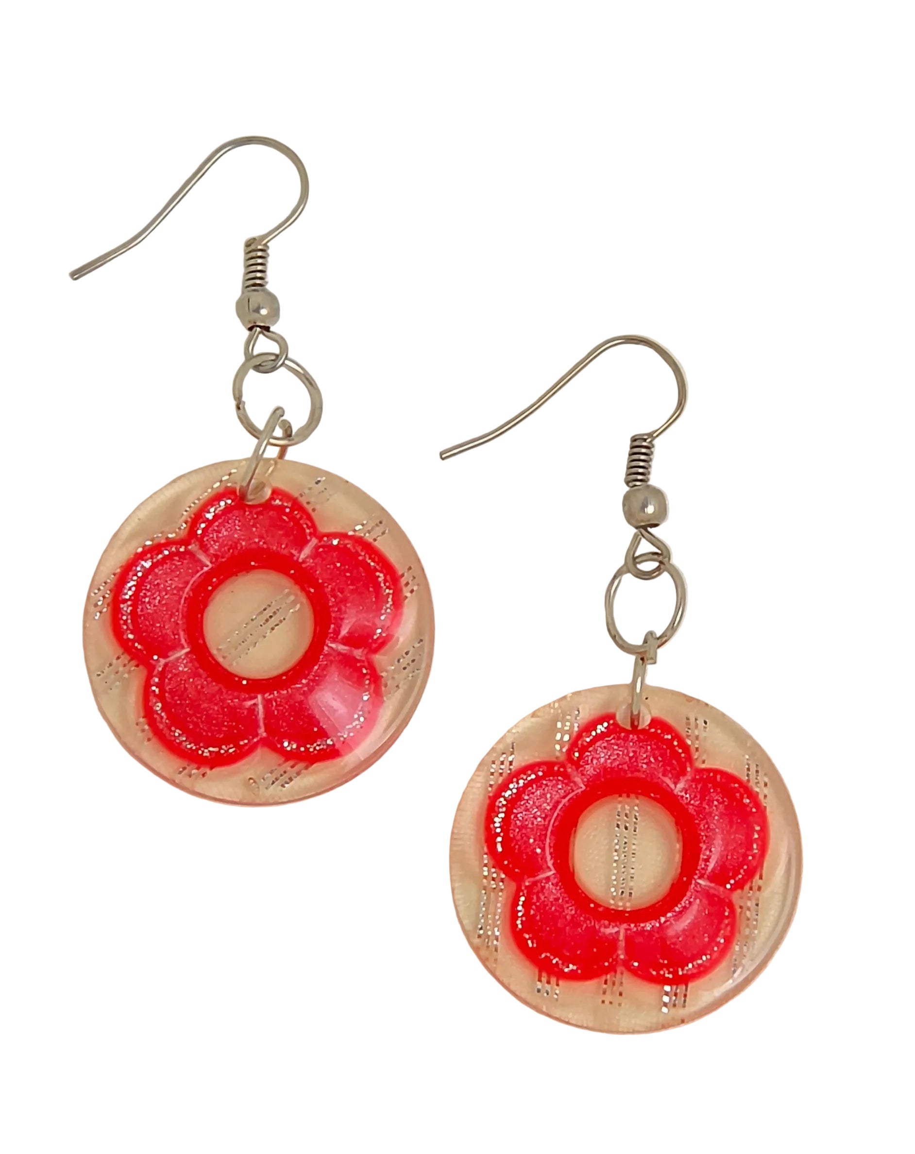 A pair of dangle earrings featuring circular translucent peach-pink resin discs with a raised red flower design in the center, suspended from silver fishhook wires on a white background.