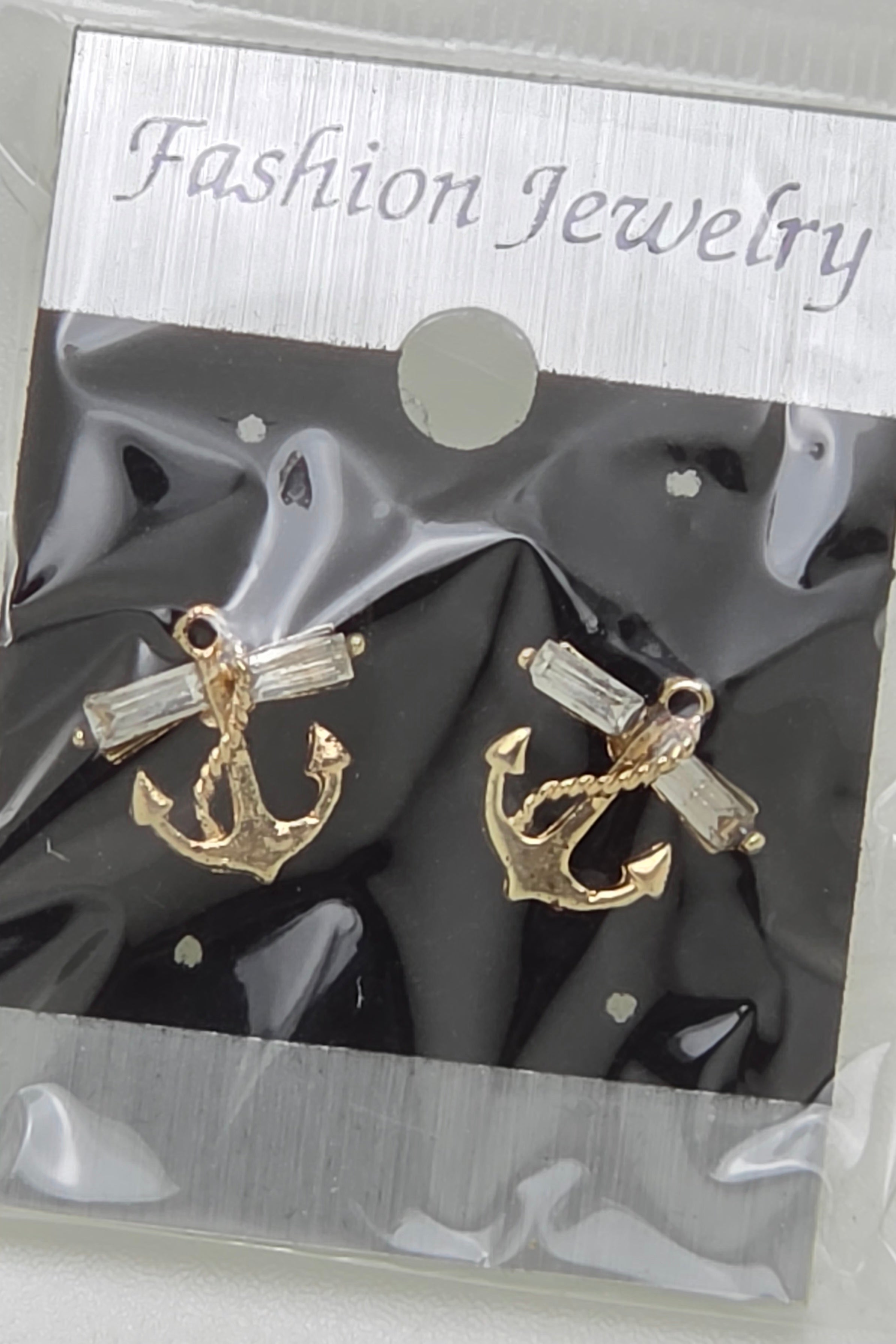 A pair of gold anchor stud earrings with clear rectangular crystals, presented on a black backing card inside a clear plastic package with a silver header that reads 'Fashion Jewelry'.