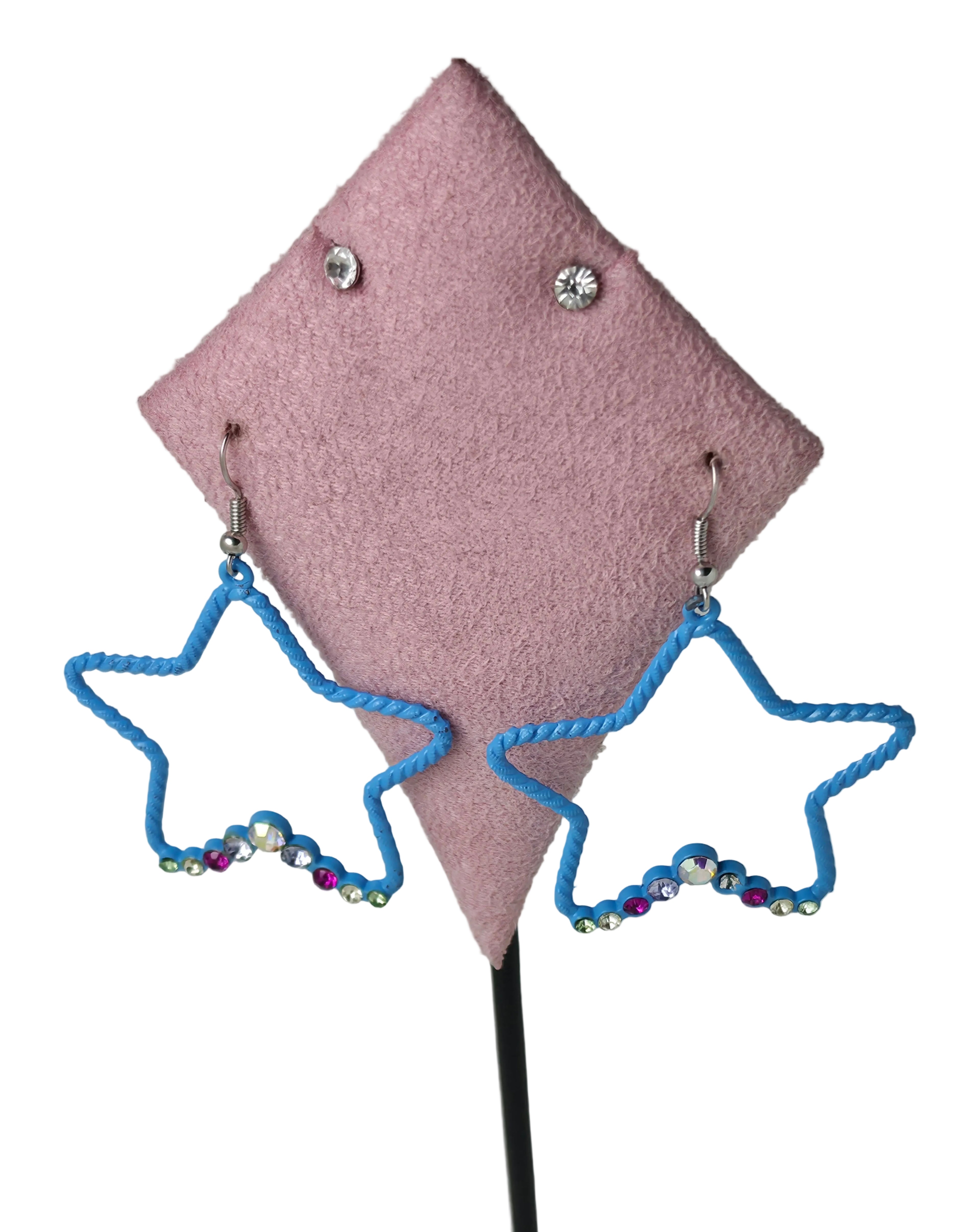 A pair of blue rope-stitched star-shaped dangle earrings with rhinestone accents, displayed on a pink felt jewelry stand against a white background.