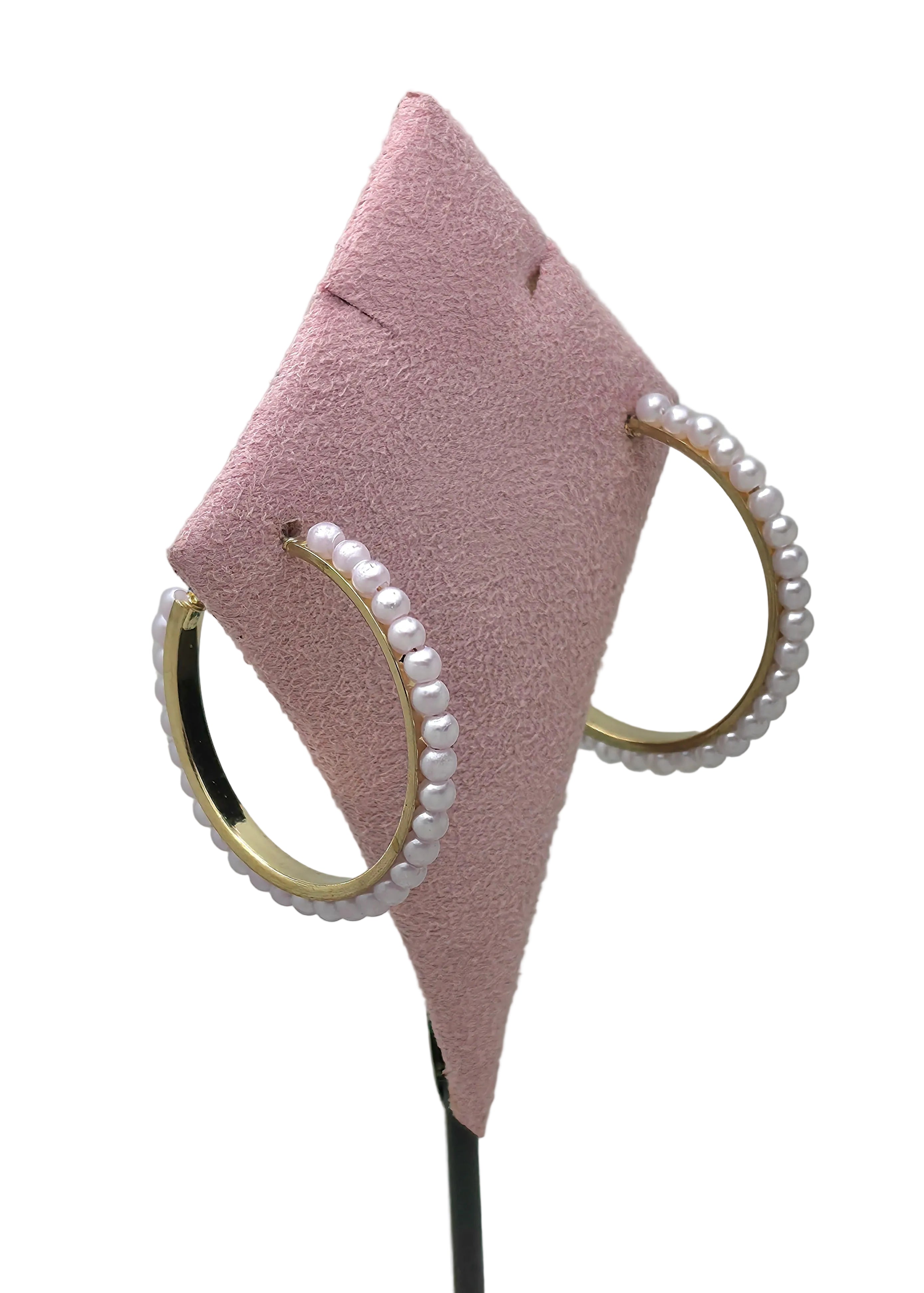 Gold-tone hoop earrings lined with white faux pearl beads displayed on pink diamond-shaped earring stand, white background, hinged closure visible