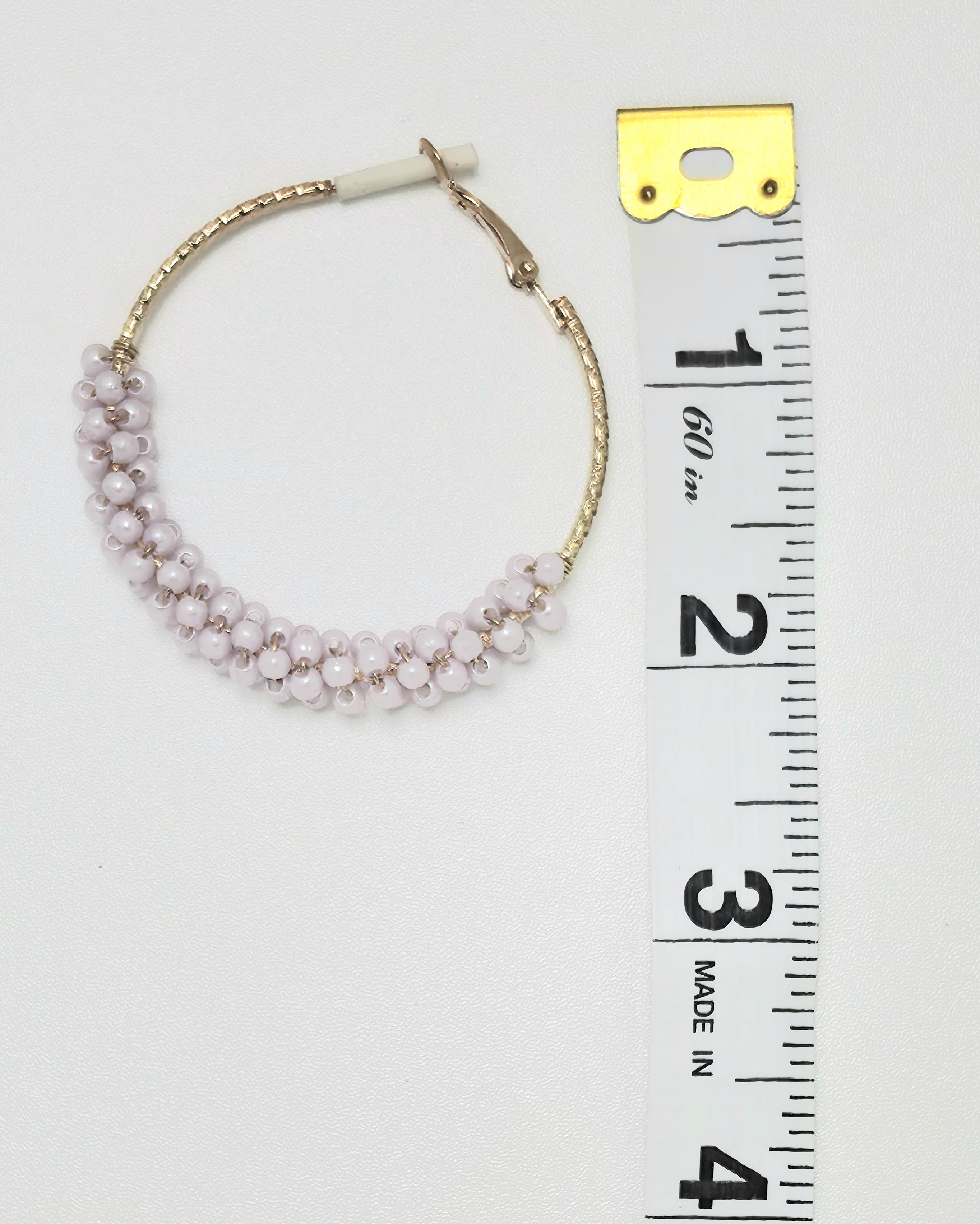 Gold crystal bead wire-wrapped hoop earring next to ruler showing approximately 2 inch diameter, lavender pink beads, hinged closure, white background