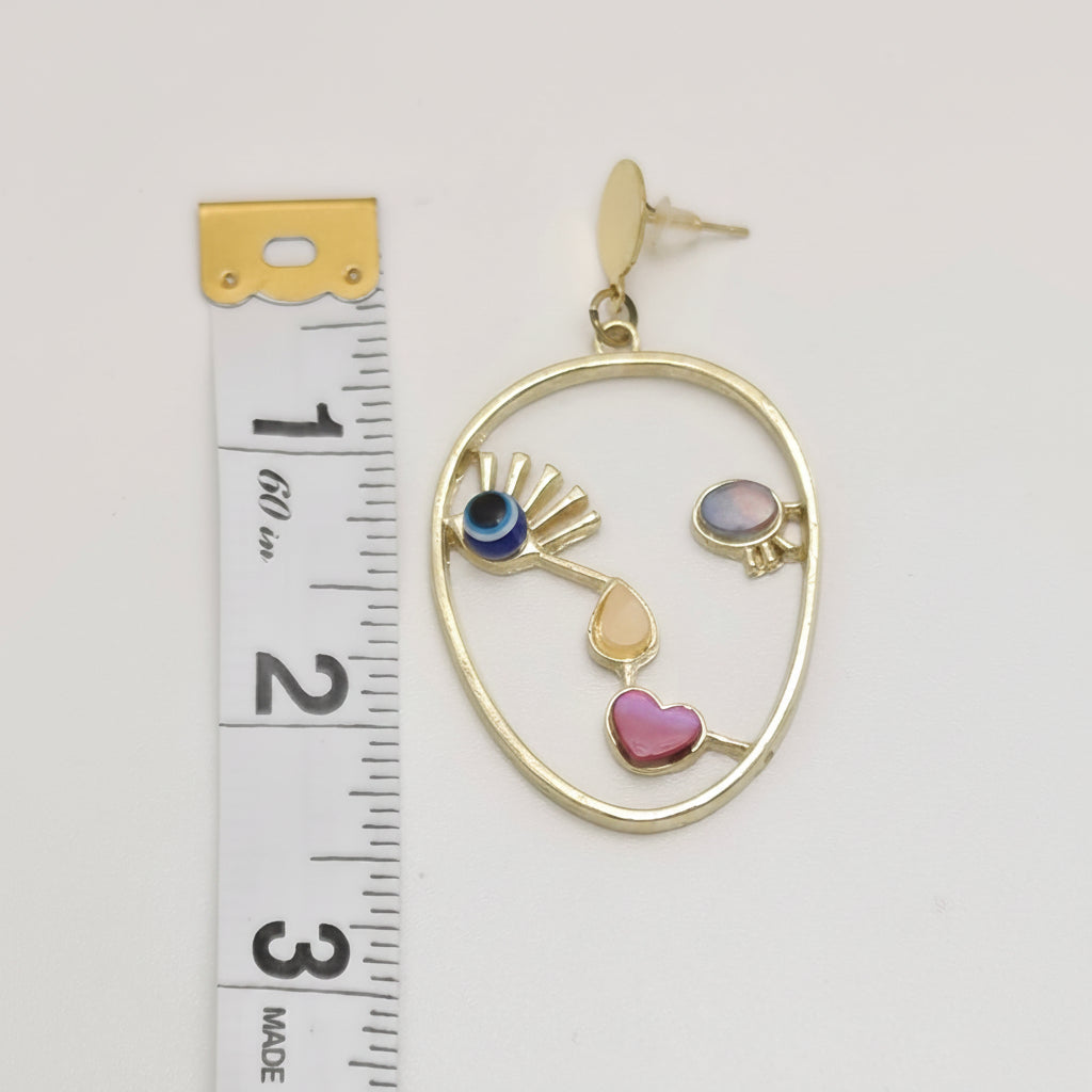 A gold-toned oval dangle earring with small colorful enamel details, shown next to a white measuring tape for scale on a white background.
