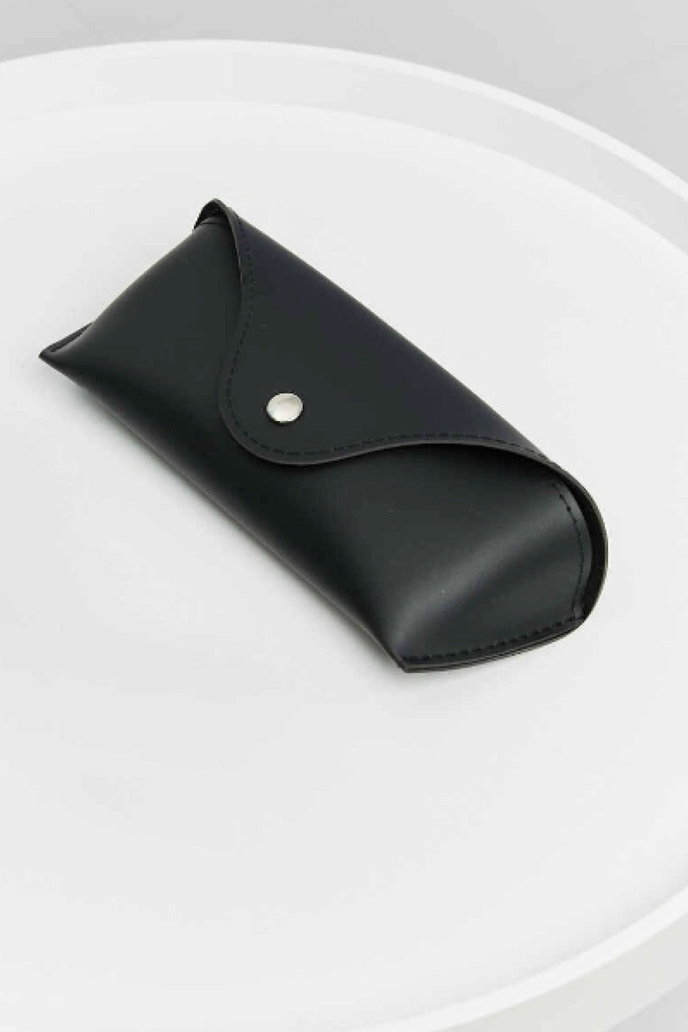 Black sunglasses case with an envelope-style flap and silver snap closure on a white surface