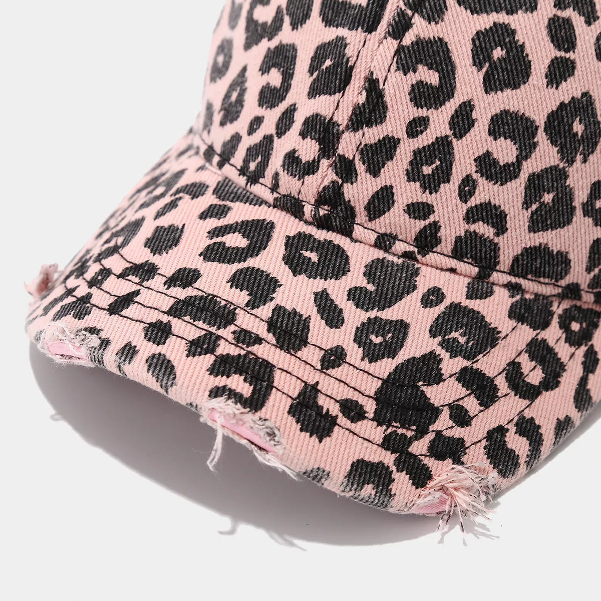 Detail of a pink-and-black leopard print baseball cap showing curved brim stitching, frayed edges, and distressed openings
