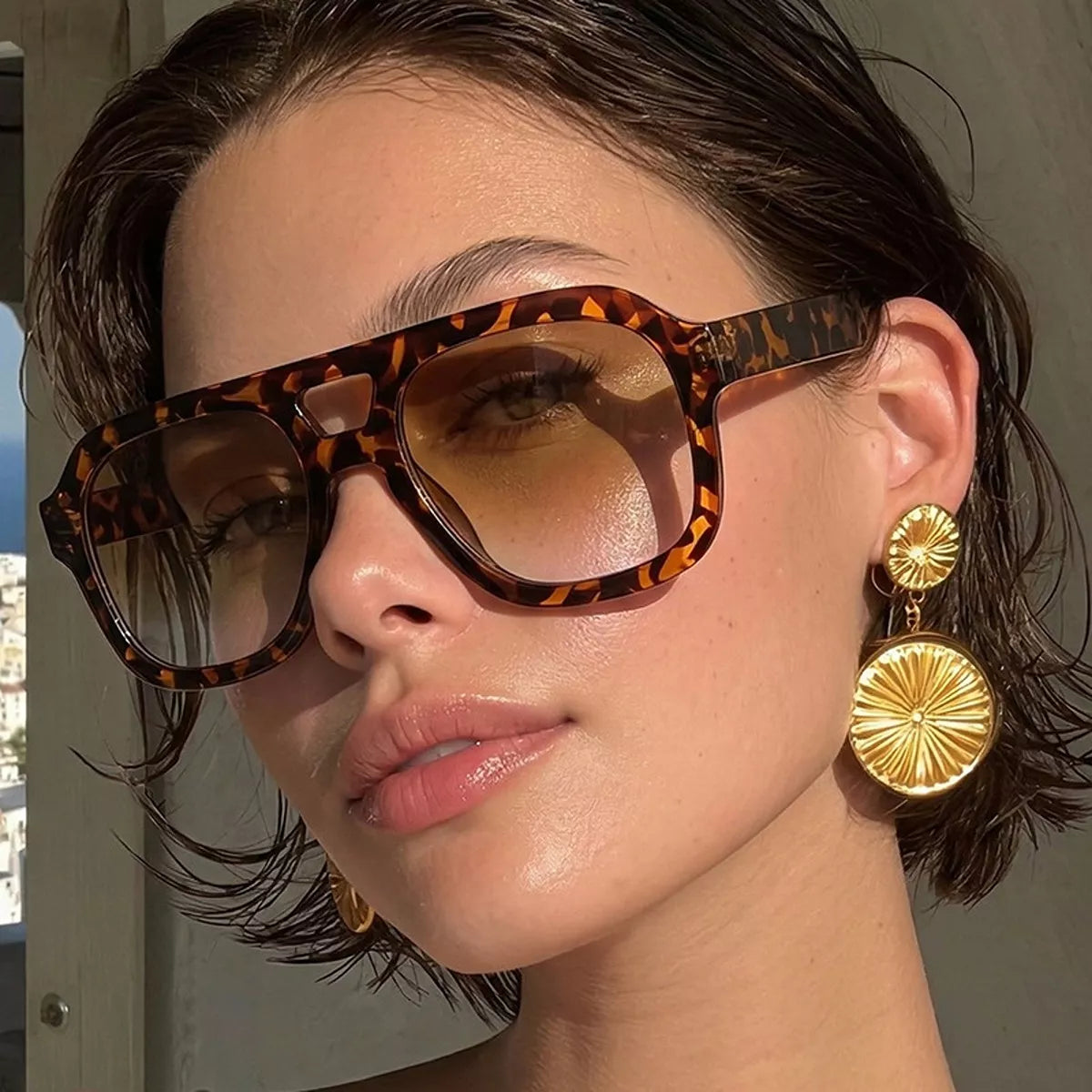 Model wearing tortoiseshell oversized aviator sunglasses with brown gradient lenses and gold-tone circular drop earrings