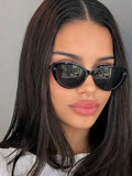 Model wearing glossy black cat-eye sunglasses with dark lenses and three-dot corner accents, styled with a light-colored top