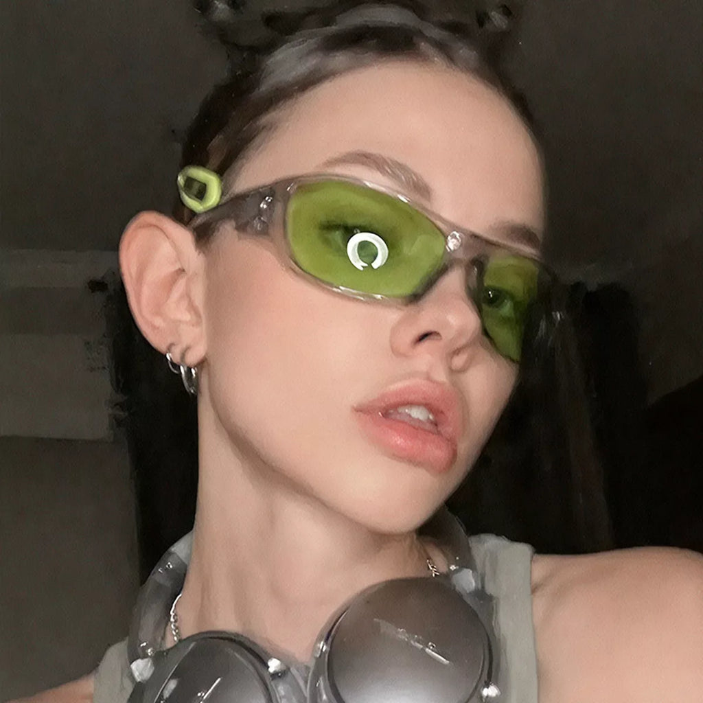 Model wearing green-tinted rectangular sunglasses with a translucent frame and silver headphones around her neck
