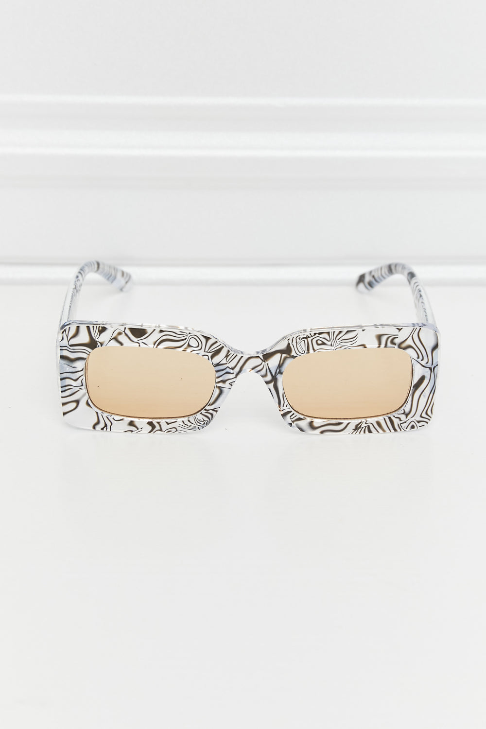 Zebra rectangle sunglasses with black-and-white swirled frames and warm-tinted lenses, shown with temples open