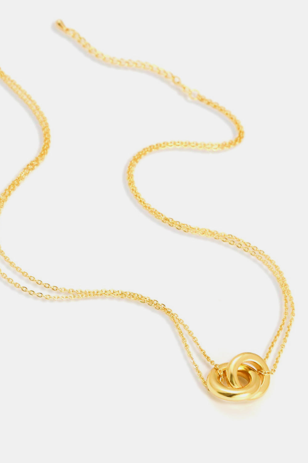 Gold-tone necklace with two interlocking rounded ring pendants and delicate chains arranged in curves on a white background