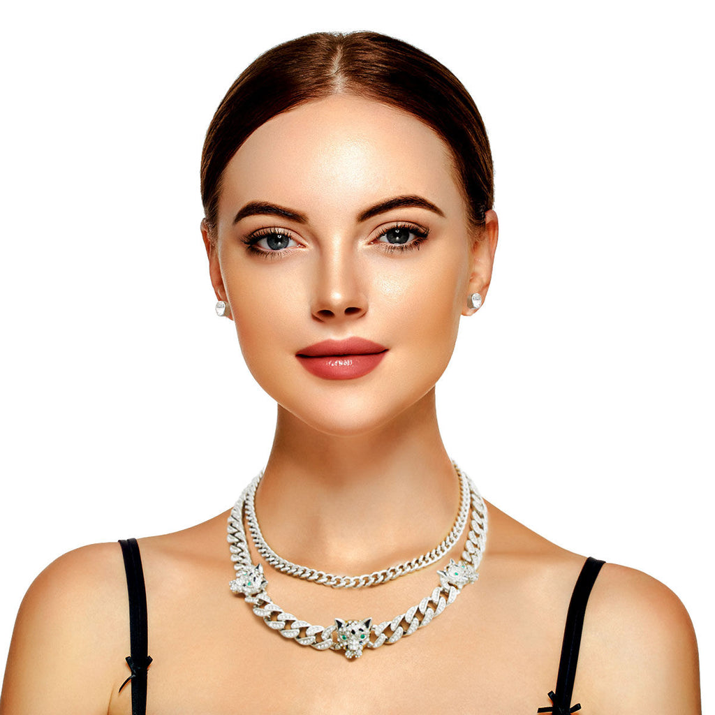 Woman wearing layered silver rhinestone iced Cuban chain necklace set with leopard station charms and green crystal eyes, black tank top, white background