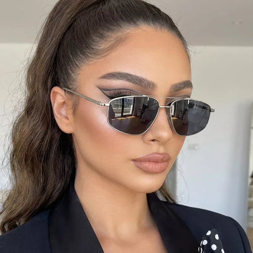 Model with a high ponytail wearing silver-tone metal aviator sunglasses with dark lenses, styled with a black blazer and polka-dot fabric detail