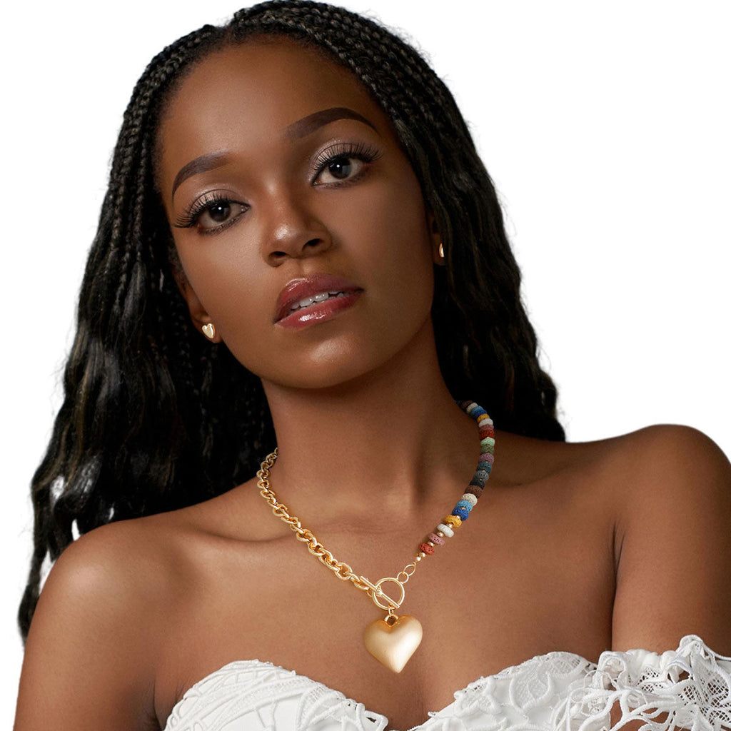 Model with braids wearing chunky multi-color bead and gold cable chain heart toggle necklace and gold heart stud earring, white strapless top