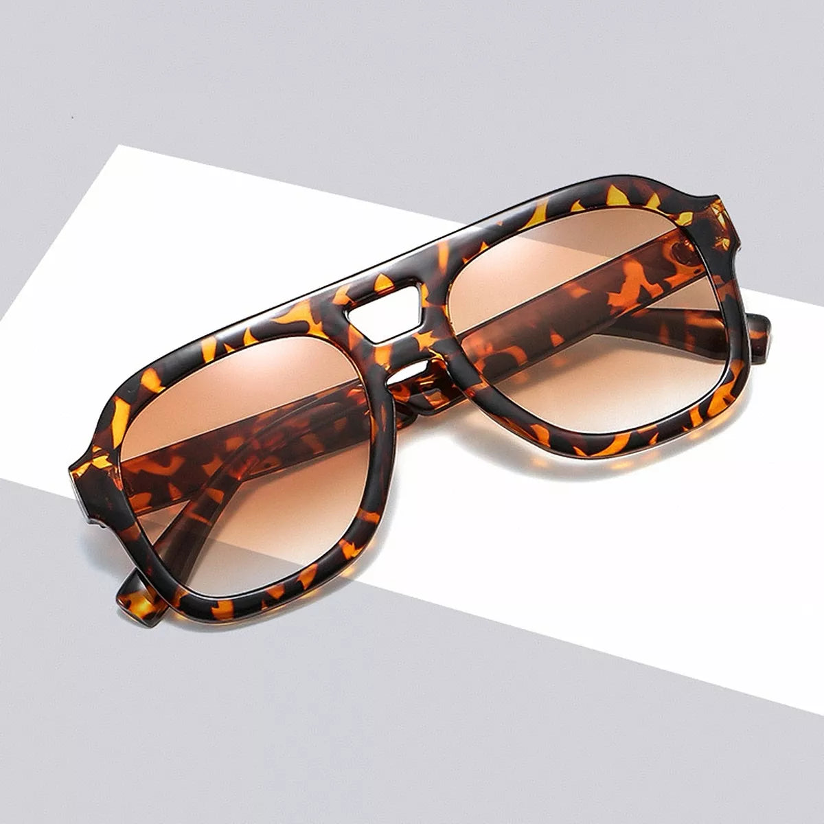 Tortoiseshell aviator sunglasses with brown gradient lenses and folded temples resting diagonally on a white display block