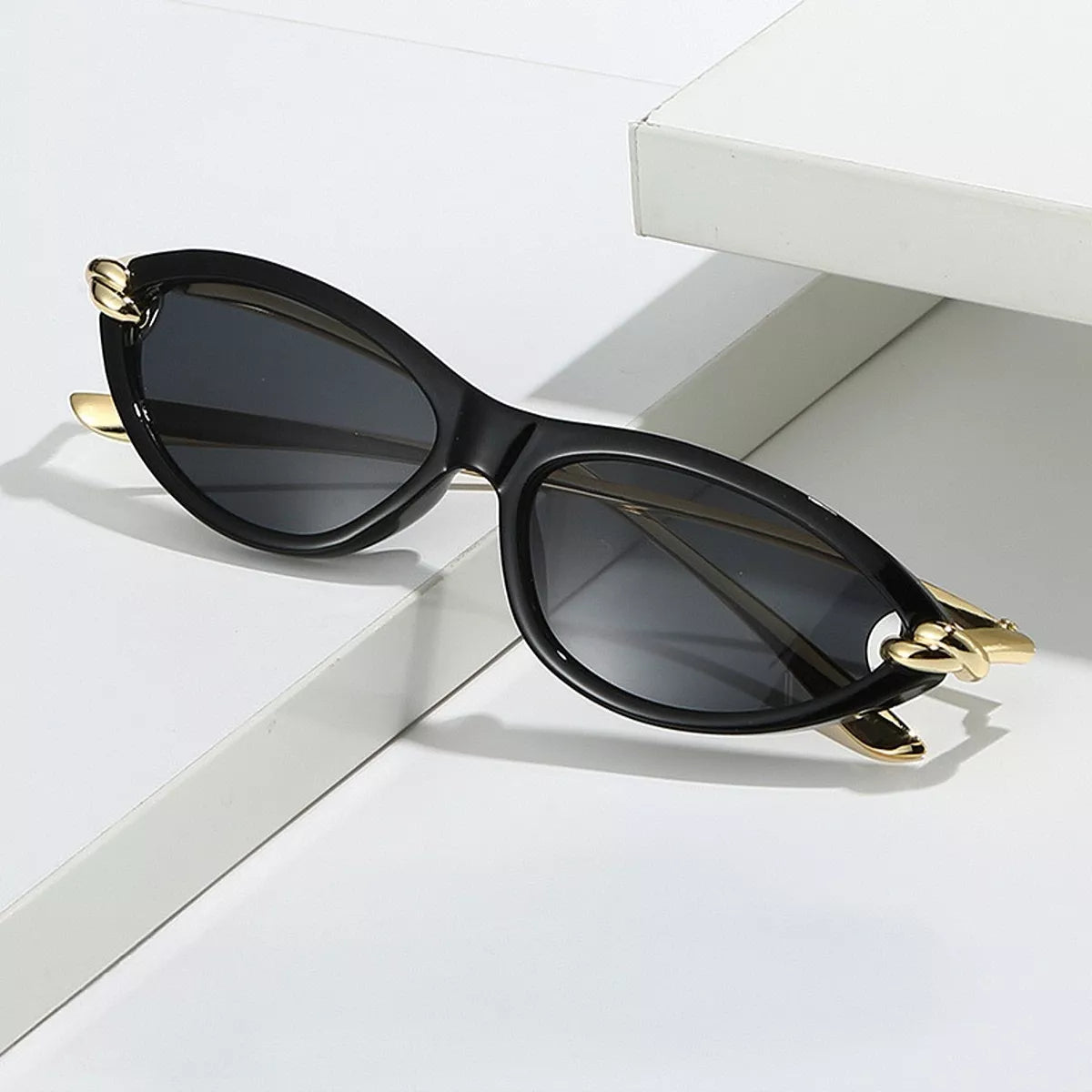 Black cat-eye sunglasses with dark lenses and gold-tone knot details resting across white display blocks