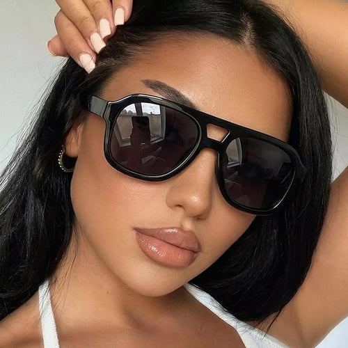 Model wearing black oversized aviator sunglasses with dark lenses, a cutout bridge, and a white top