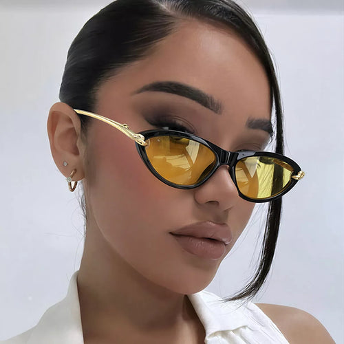 Model wearing black cat-eye sunglasses with yellow lenses and gold-tone temples, styled with a white collared top