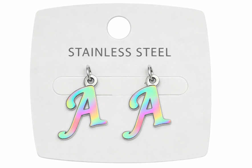 A pair of stainless steel initial earrings shaped like the letter 'A', featuring an iridescent pastel rainbow finish, displayed on a white backing card labeled 'STAINLESS STEEL'.