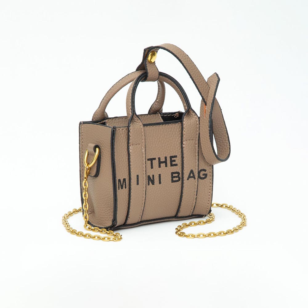 A miniature taupe faux-leather handbag with black text reading 'THE MINI BAG' on the front, featuring gold-tone hardware, a gold chain strap, and black trim, set against a plain white background.