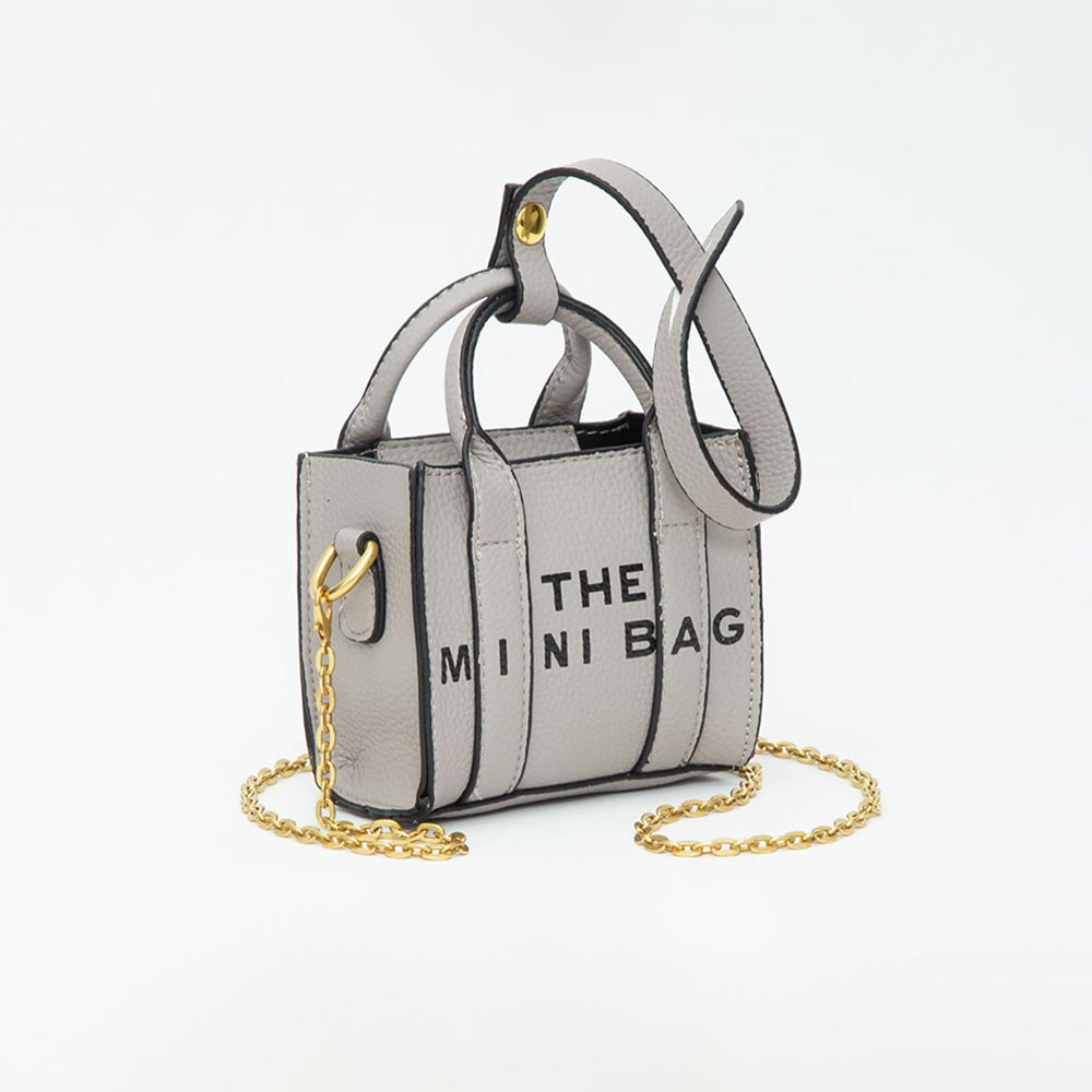A miniature gray faux-leather handbag with black text reading 'THE MINI BAG' on the front, featuring dual top handles, a gold-tone chain strap, and gold hardware, photographed on a white background.