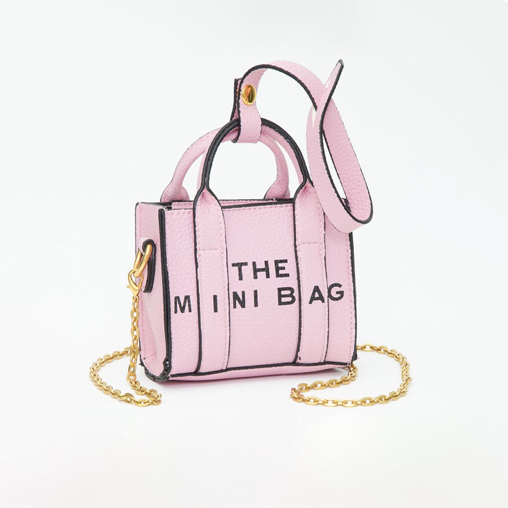 A small pink faux-leather handbag with black trim, gold chain strap, and black text reading 'THE MINI BAG' on the front, photographed on a clean white background.