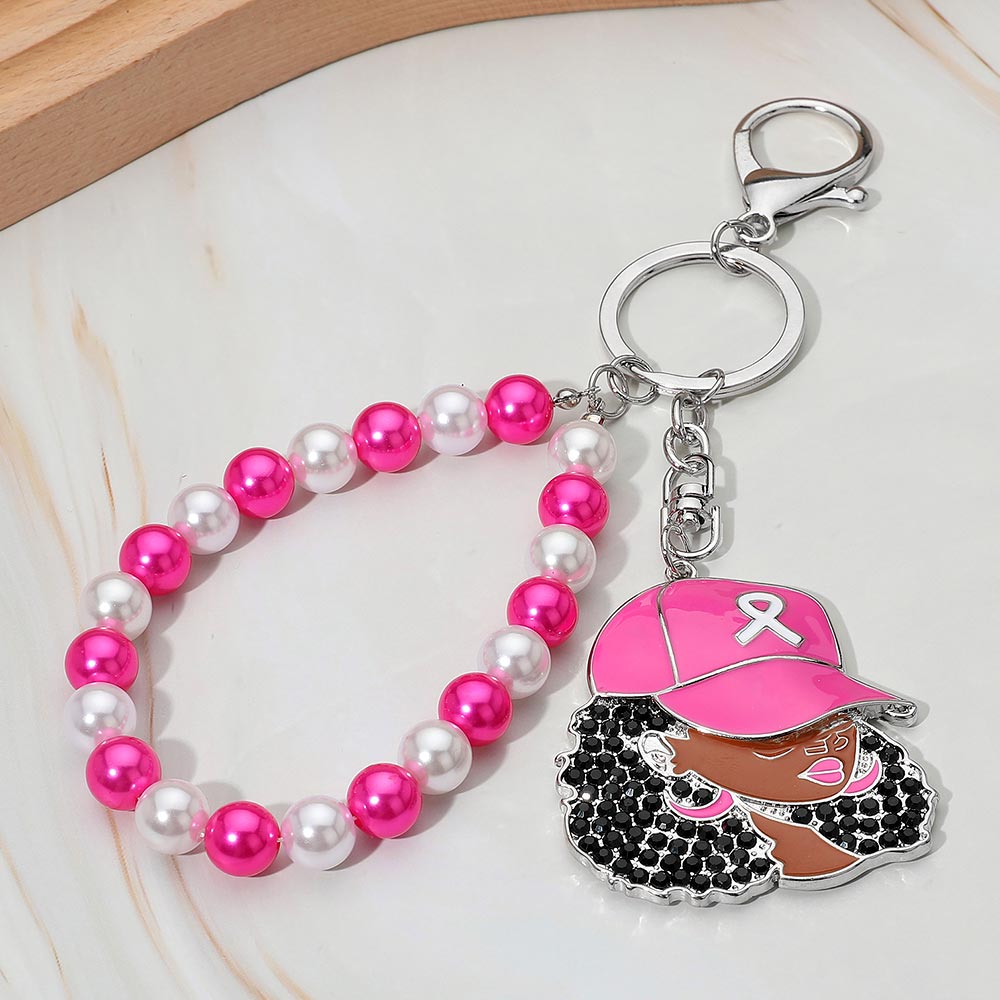Black rhinestone-paved Afro woman enamel charm with pink cap and white awareness ribbon, attached to hot pink and white pearl beaded wristlet loop with silver lobster clasp and split ring, displayed on white marble surface