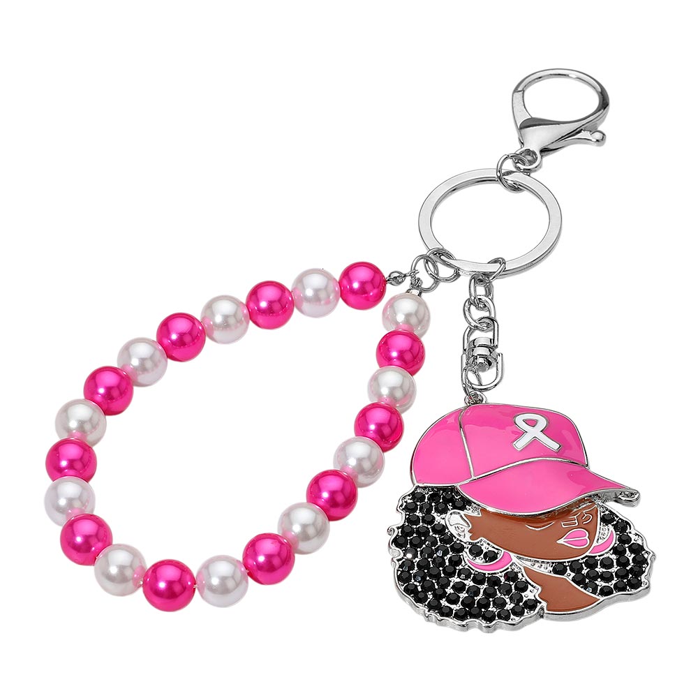 Women's Afro rhinestone bag charm keychain with pink enamel baseball cap and white awareness ribbon, black crystal-paved hair and brown skin tone, connected to alternating hot pink and white pearl beaded wristlet with silver lobster clasp hardware, white background