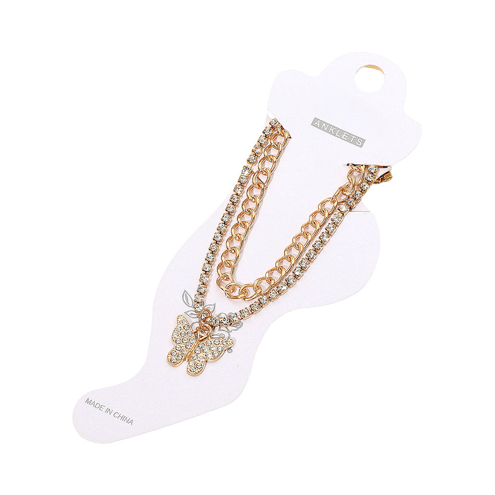 Rhinestone pavé butterfly charm layered chain anklet in gold-tone displayed on white foot-shaped retail card — gold curb chain and rhinestone tennis chain layers, rhinestone pavé butterfly pendant with leaf charm, gold lobster clasp, white background