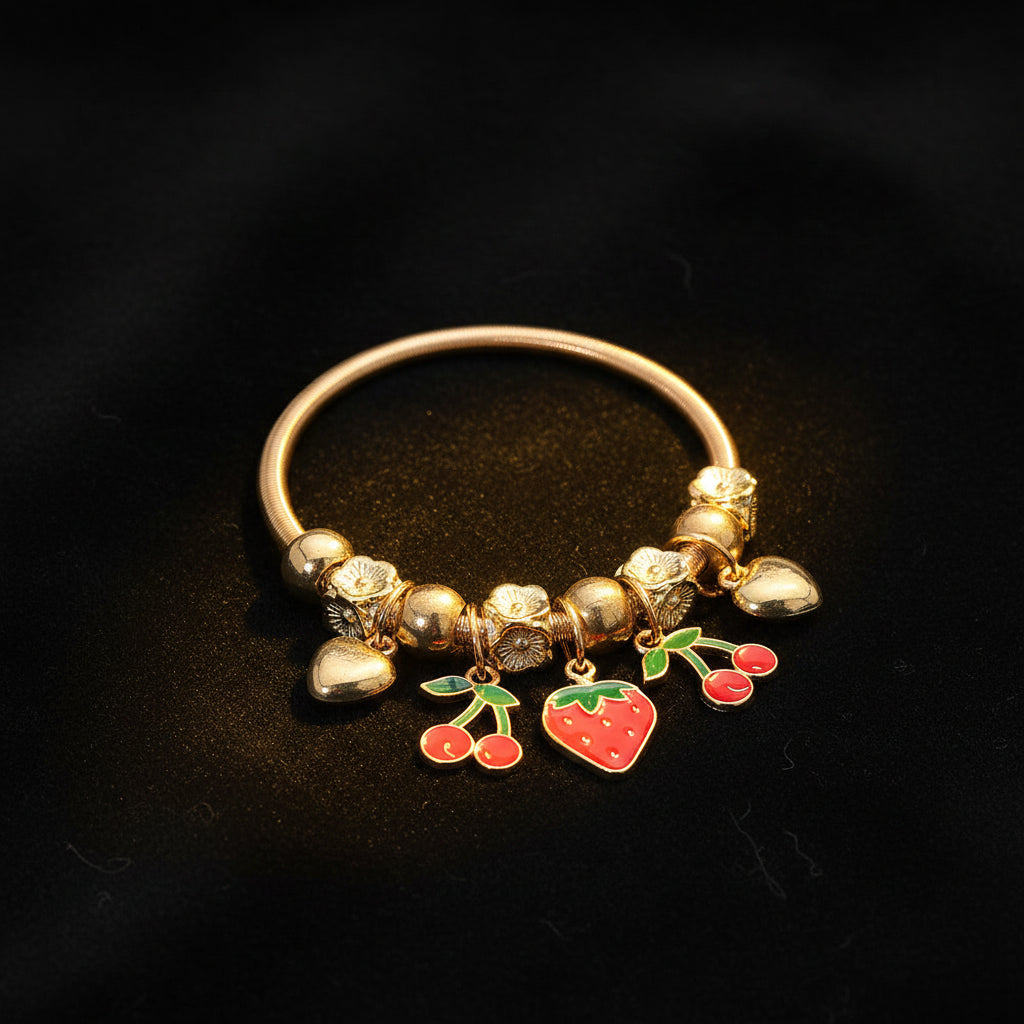 Gold-tone charm stretch bracelet with engraved flower bead spacers and gold ball beads, featuring dangling red enamel cherry charms with green leaves, red enamel strawberry charm, and gold heart charm, dark background