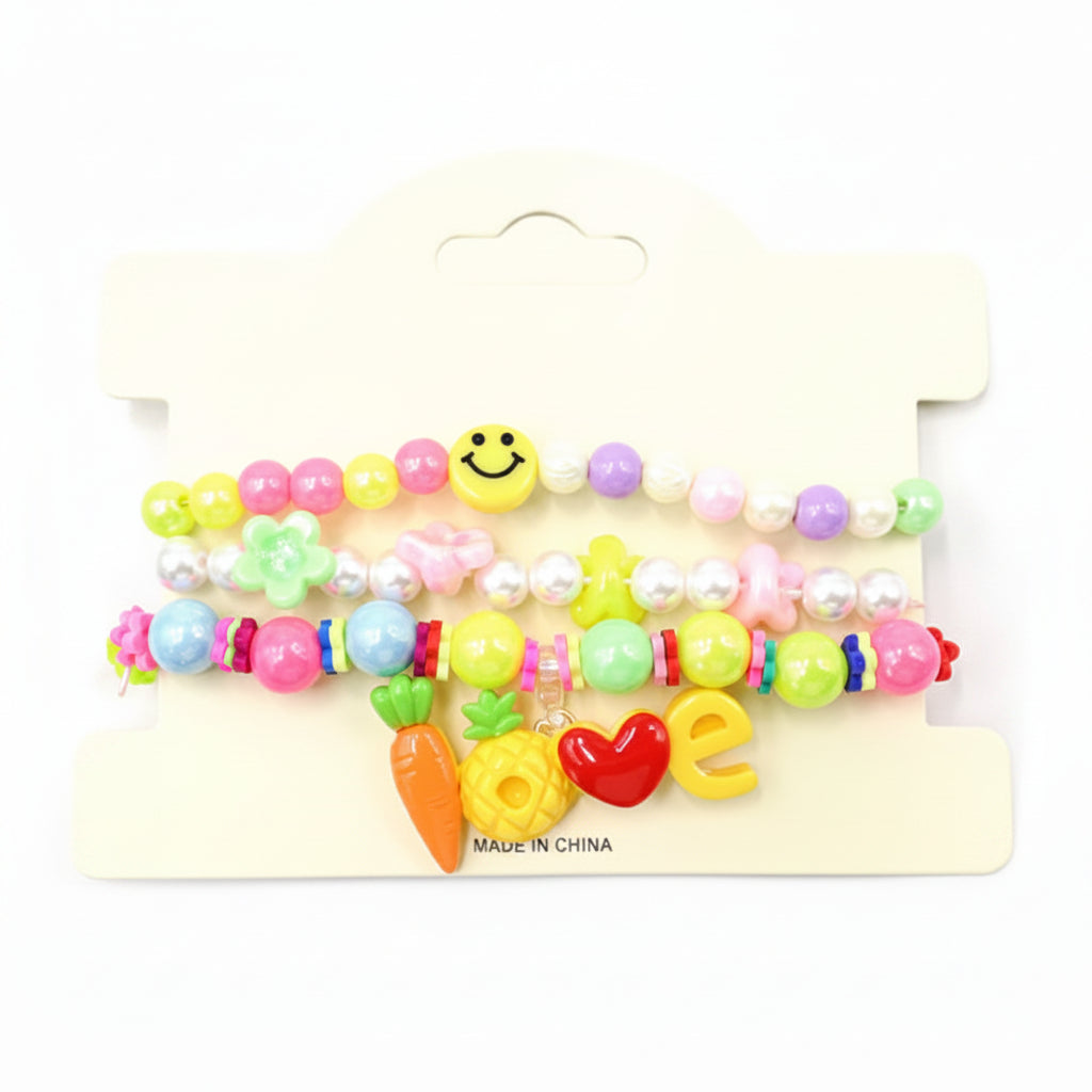 Kids charm beaded stretch bracelet set in bright multicolor — 3-piece stackable set with rainbow bead bracelet with smiley face, pearl bead bracelet with flower and star charms, and LOVE charm bracelet with carrot, pineapple, heart, and letter charms, cream retail card, white background