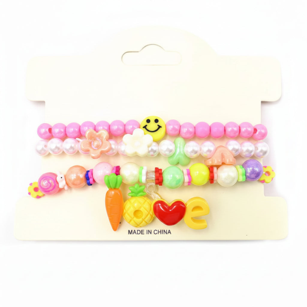 Kids charm beaded stretch bracelet set in pink and multicolor — 3-piece stackable set with pink bead bracelet with smiley face, pearl bead bracelet with flower charms, and LOVE charm bracelet with carrot, pineapple, heart, and letter charms and flamingo accent bead, cream retail card, white background