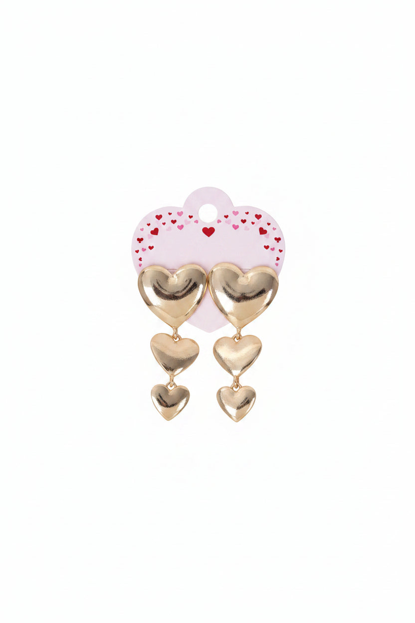 Triple metal heart link dropdown earrings in polished gold-tone on pink heart-shaped retail card with red heart confetti print — large puffy heart post stud at top with two cascading smaller puffy heart charms linked by gold jump rings, white background
