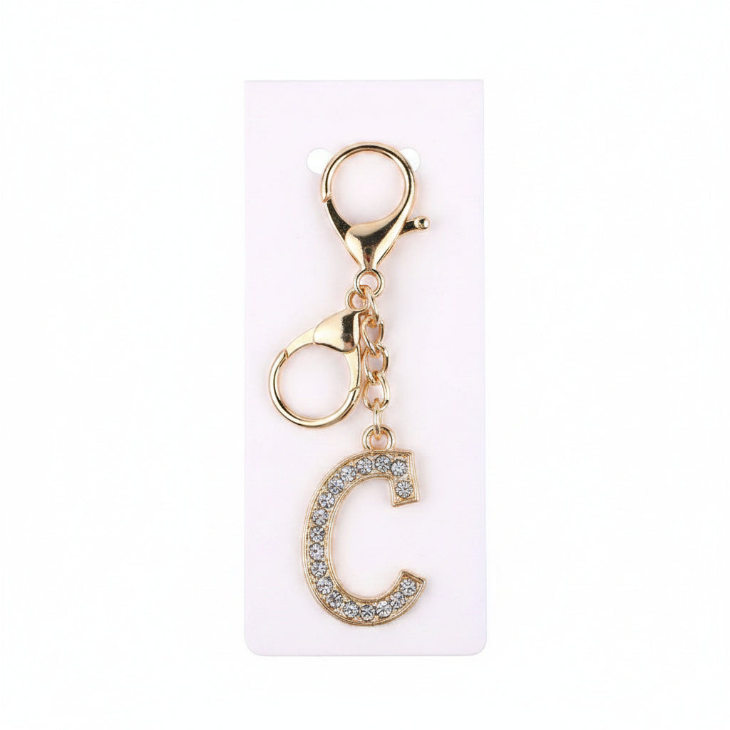 Rhinestone pavé initial letter C keychain bag charm with clear crystal rhinestone pavé block C pendant, gold-tone lobster clasp and gold chain link, displayed on white retail card, white background