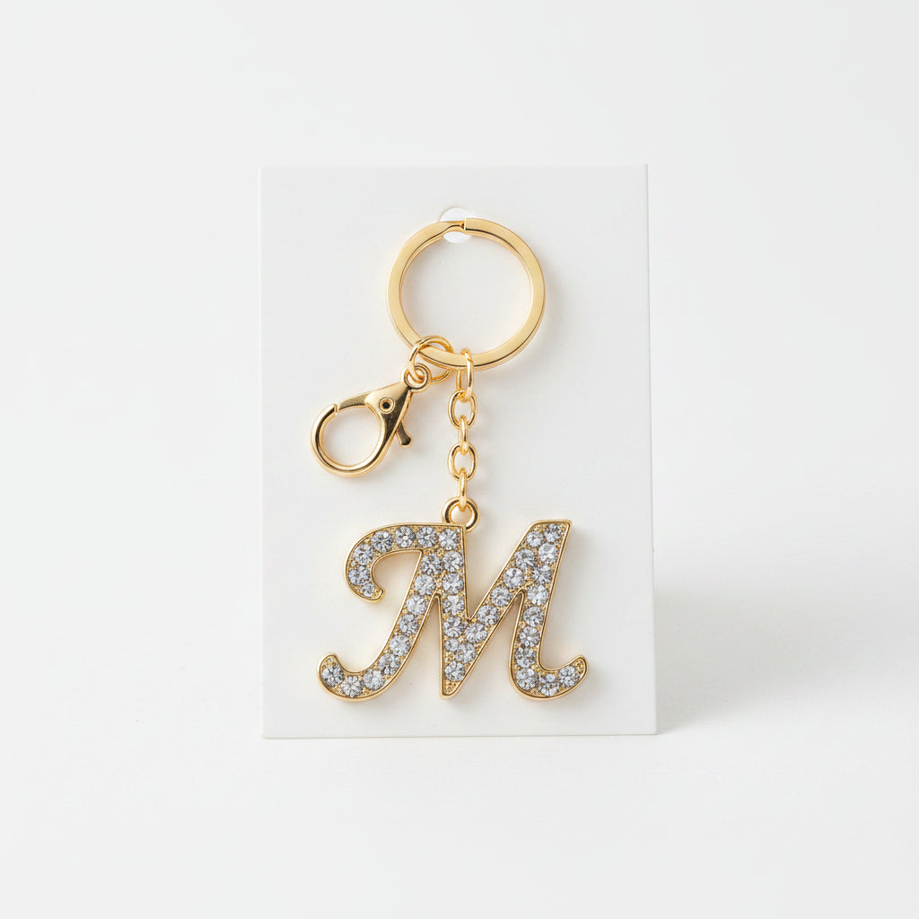 Rhinestone pavé initial letter M keychain bag charm with clear crystal rhinestone pavé script M pendant, gold-tone lobster clasp and key ring, displayed on white card with soft gray background