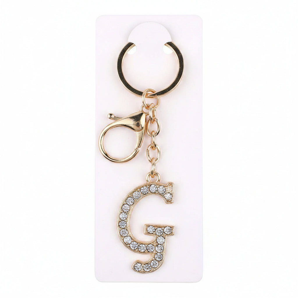 Rhinestone pavé initial letter G keychain bag charm with clear crystal rhinestone pavé G pendant, gold-tone lobster clasp and key ring, displayed on white retail card, white background