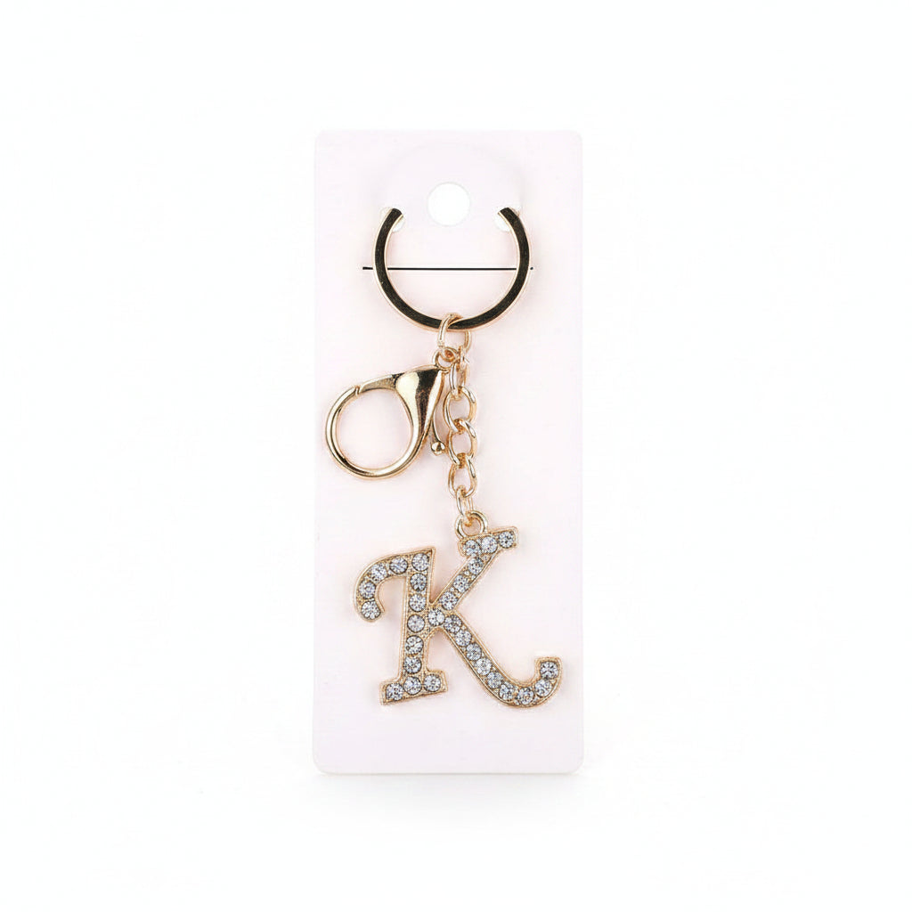 Rhinestone pavé initial letter K keychain bag charm with clear crystal rhinestone pavé script K pendant, gold-tone lobster clasp and key ring, displayed on white retail card, white background