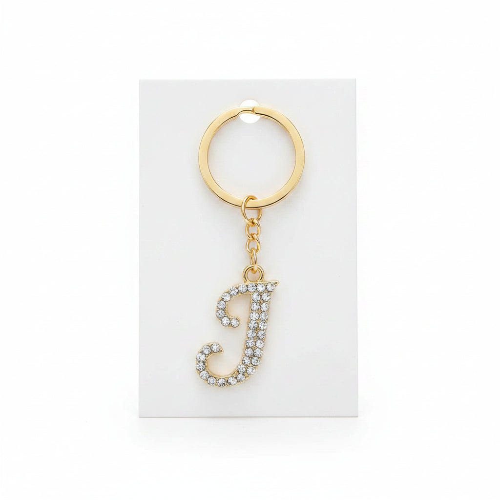 Rhinestone pavé initial letter J keychain bag charm with clear crystal rhinestone pavé script J pendant, gold-tone key ring and gold chain link, displayed on white retail card, white background
