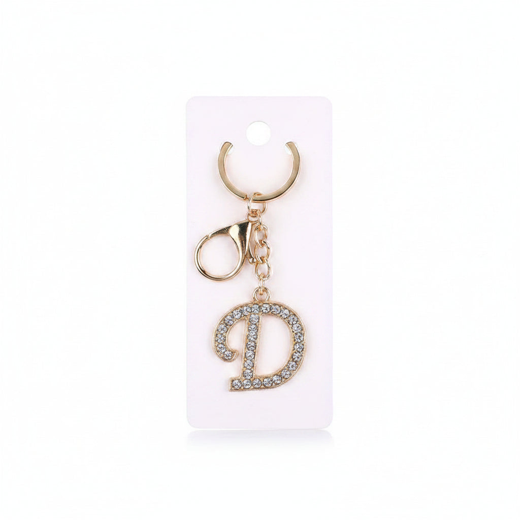 Rhinestone pavé initial letter D keychain bag charm with clear crystal rhinestone pavé script D pendant, gold-tone key ring and lobster clasp with gold chain link, displayed on white retail card, white background