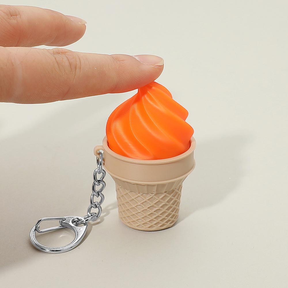 Finger pressing down on orange soft-serve swirl top of plastic ice cream cone fidget clicker keychain with tan waffle cone base and silver chain with lobster clasp, demonstrating squeeze mechanism, cream background